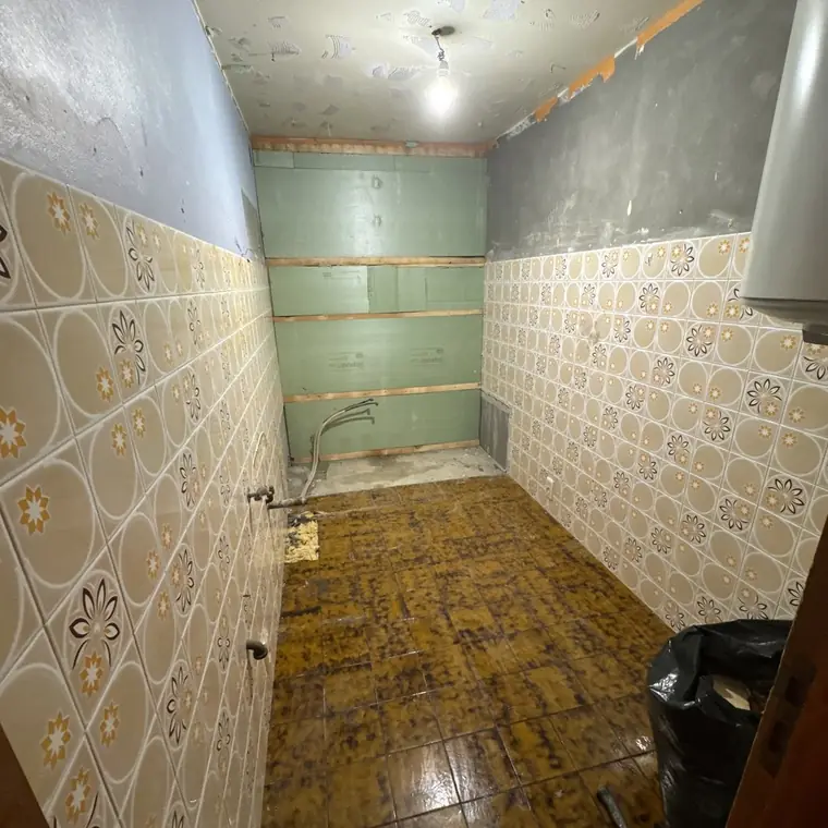 Ancienne salle de bain au carrelage mural à motifs, cloison ouverte sur les arrivées d’eau