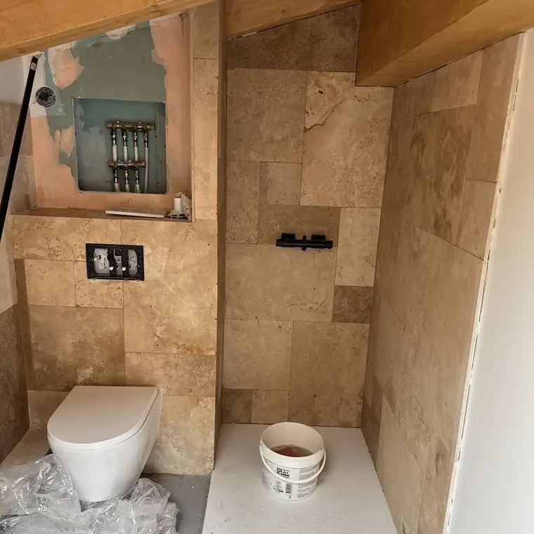Salle d’eau en travertin sous rampant avec poutres apparentes