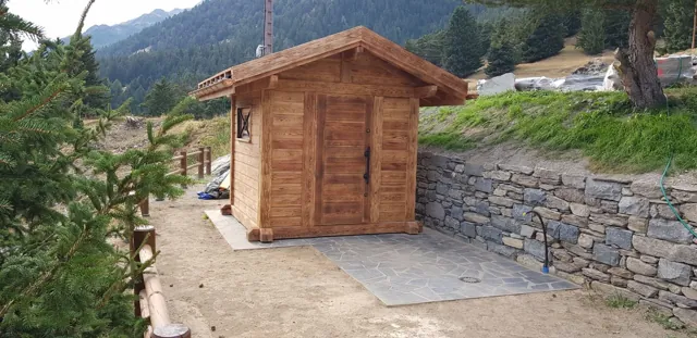 Petit abri en bois au pied d’un mur en pierre, montagnes au fond