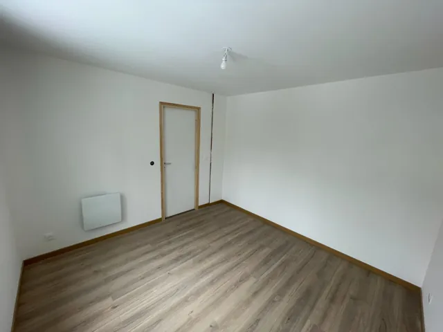 Chambre vide aux murs blancs et au sol stratifié, radiateur au mur