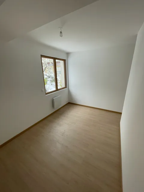 Chambre vide aux murs blancs, sol stratifié et fenêtre en bois