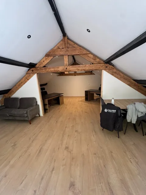 Grande pièce sous combles avec charpente en bois apparente, plafond blanc et spots encastrés