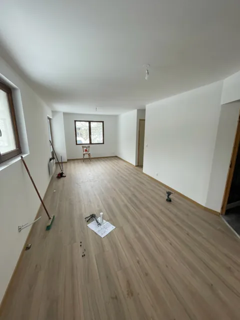 Pièce en fin de chantier, murs blancs et sol stratifié, quelques outils au sol