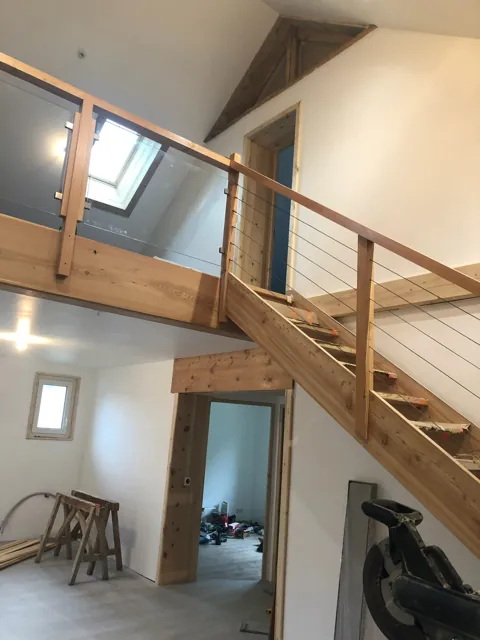 Mezzanine en bois desservie par un escalier, garde-corps à câbles, fenêtre de toit