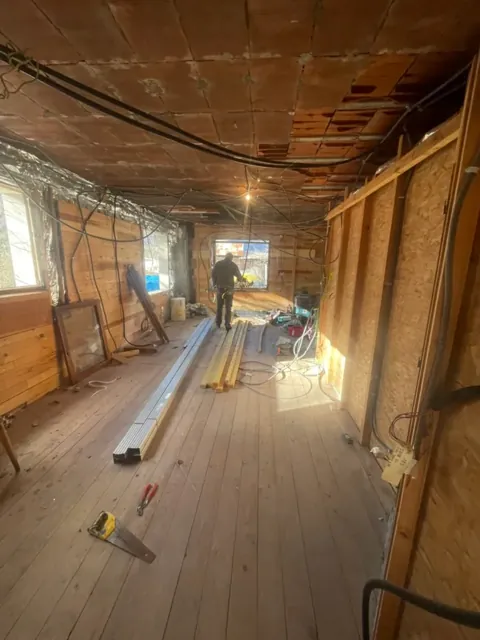 Pièce en cours de rénovation : ossature bois et panneaux OSB, câbles électriques au plafond, un compagnon au fond
