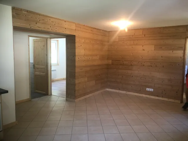 Pièce aux murs en lambris clair et au sol carrelé, porte ouverte sur une autre pièce
