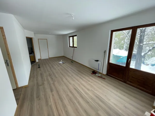 Séjour en fin de chantier avec porte-fenêtre en bois, sol stratifié, outils au sol