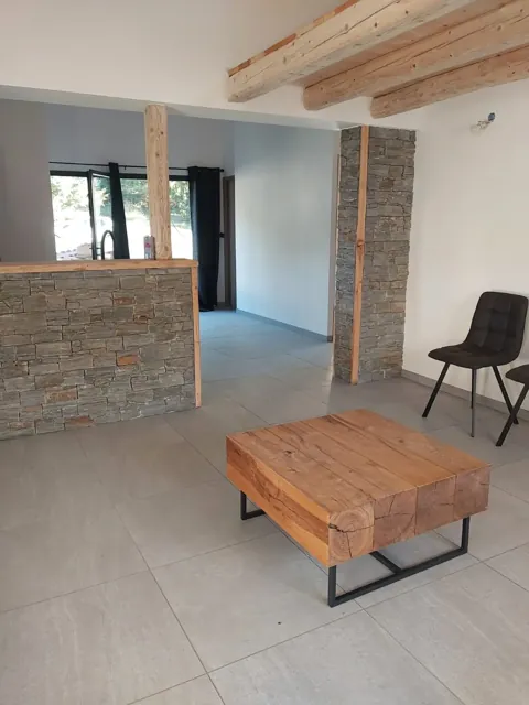 Séjour avec bar et poteau habillés de pierre de parement, poutres en bois au plafond, carrelage gris grand format